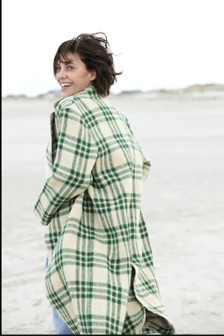 Frau im karierten Mantel am Strand lächelnd