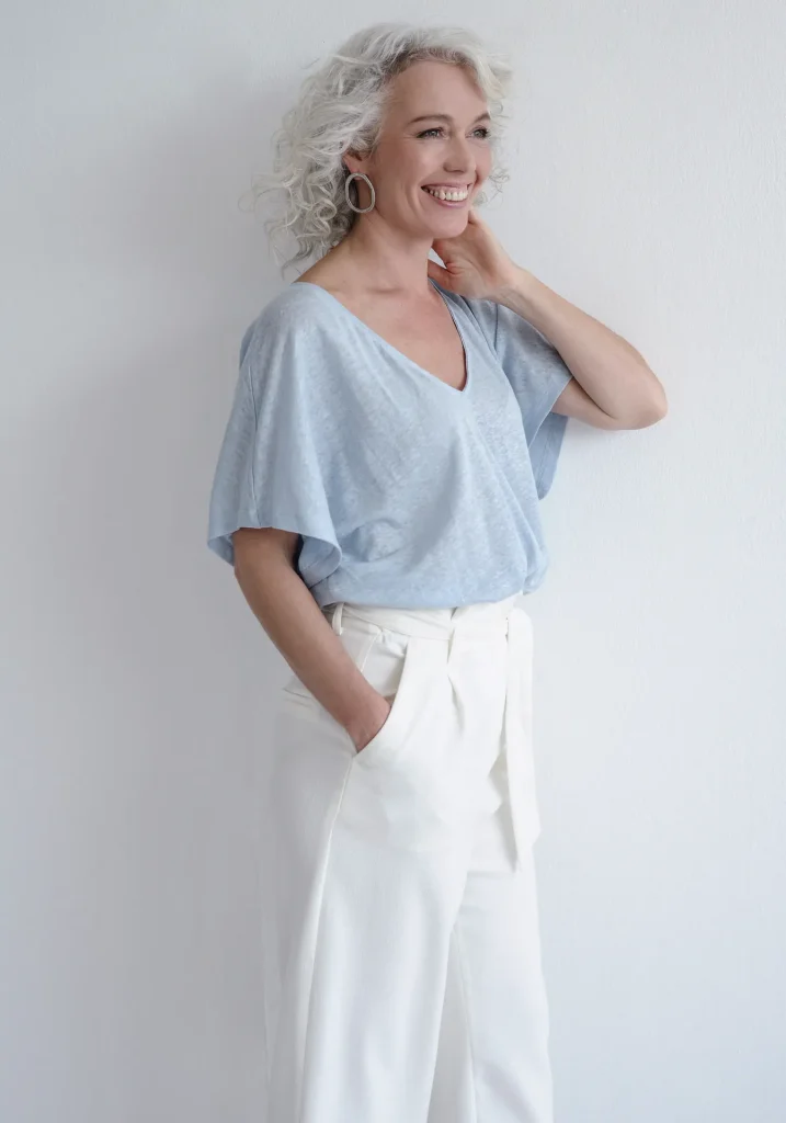 Lächelnde Frau mit grauen Locken in hellem Outfit