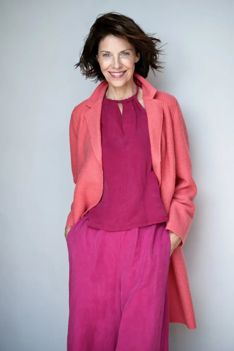 Lächelnde Frau im pinken Outfit vor grauem Hintergrund
