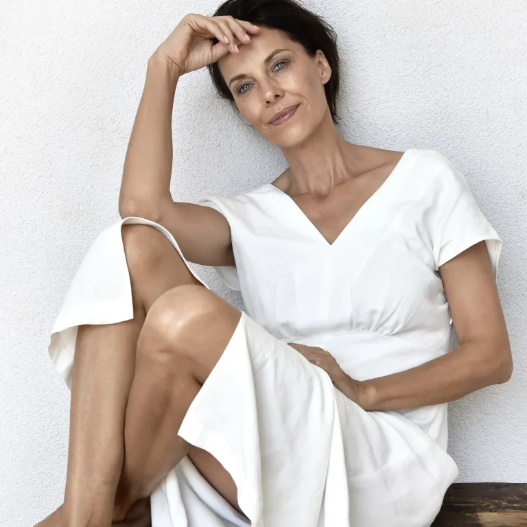 Elegante Frau in weißem Kleid an Wand