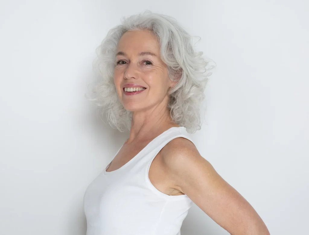 Lächelnde Frau mit grauen Locken im weißen Top