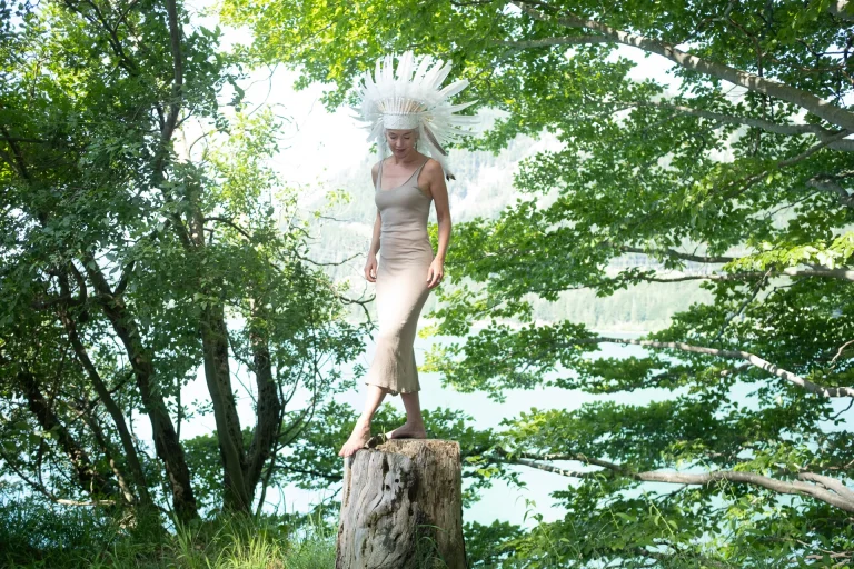 Frau mit Federkopfschmuck auf Baumstumpf am See