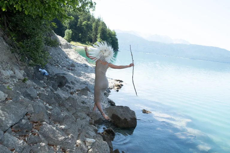 Person mit Federkopfschmuck am Seeufer